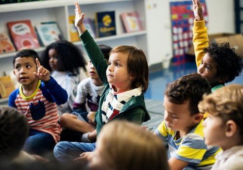 young kids raising their hands at preschool